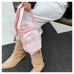 Close-up of a light pink nylon crossbody bag with drawstring and zip pockets