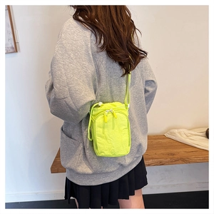 Detail of neon green crossbody sports bag showing drawstring closure and zipper pocket