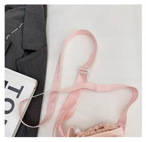 Detail of adjustable nylon shoulder strap and white buckle on pale pink crossbody bag