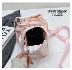 Front zipper pocket of a light pink nylon crossbody bag showing smartphone storage