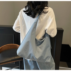 Rear view of a model wearing a large light blue nylon crescent crossbody tote bag