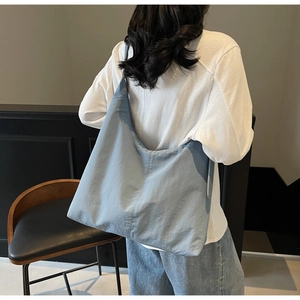Rear view of a large grey-blue crescent tote bag with soft pleated texture on a model