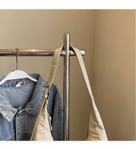 Detail of beige canvas tote bag with long shoulder straps shown on a metal hanger