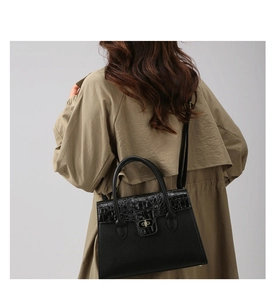 Detail einer schwarzen Handtasche in Krokodil-Optik mit goldenem Drehverschluss am Model
