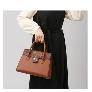 Detail einer braunen Handtasche mit Krokodilmuster und metallischem Drehverschluss-Design