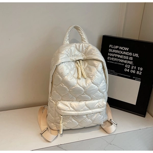 Close-up of white quilted puffer backpack with heart patterns on a marble surface