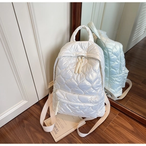 Detail of white quilted backpack with heart pattern and rope zipper pulls in a cozy setting