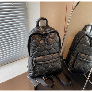 Detailed close-up of black quilted puffer backpack with diamond stitching and front zip pocket