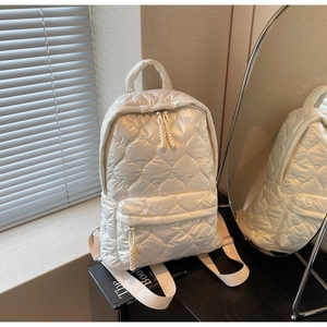 Detail of white heart-quilted puffer backpack with woven cord zipper and front pocket