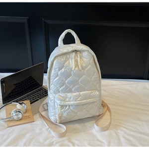 Close-up of white quilted puffer backpack with embroidered texture and casual workspace decor