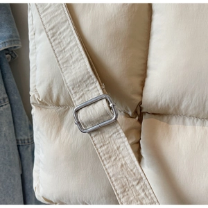 Detail of beige quilted puff bag featuring a wide shoulder strap and silver metal buckle