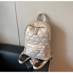 Detailed close-up of champagne gold quilted backpack with woven zipper pulls on a magazine