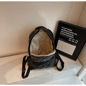 Detail of black quilted backpack featuring embroidered diamond pattern and wide inner opening