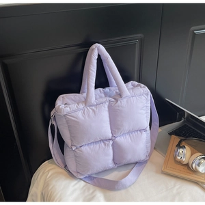 Detail of lavender quilted puffer bag on white bedding with minimalist laptop decor
