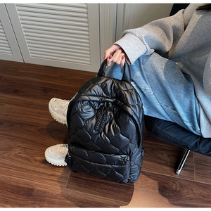 Close-up of black quilted down backpack featuring wavy stitching and a stylish side zipper