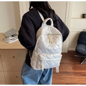 Detailed view of white quilted puffer backpack with heart patterns and woven zipper cord