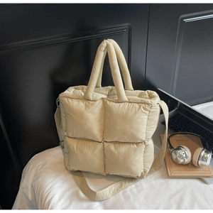 Detail of soft quilted cream tote bag with padded handles and adjustable strap on bed