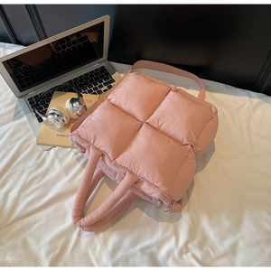 Pink quilted puffer tote bag with handles and adjustable strap on white bedding scene