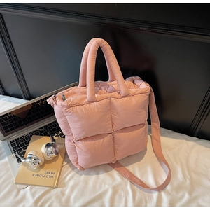 Detail of pink quilted puffer bag with adjustable strap next to a laptop and books