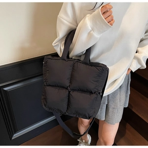 Close-up of a black quilted puffer tote bag with puffy down-filled squares and straps