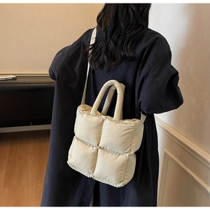 Detail of beige quilted puffer tote bag on shoulder with navy coat for winter style