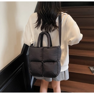 Detail of a black quilted down tote bag worn on shoulder over a casual outfit