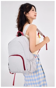 Detail view of foldable light grey travel backpack with maroon straps on a model back