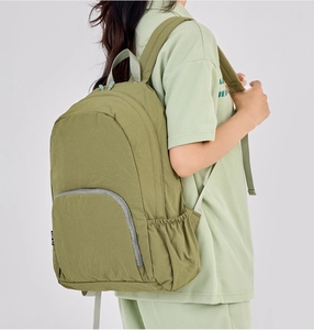 Side view of olive green ultralight foldable backpack worn by model on grey background