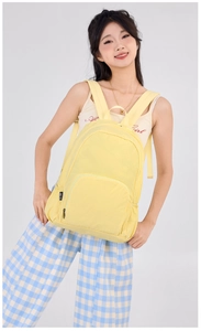 Detail of bright yellow lightweight folding backpack featuring front pocket and side woven label