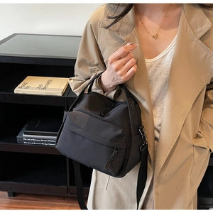 Detail der schwarzen Nylontasche mit verstellbarem Gurt kombiniert mit beigem Trenchcoat