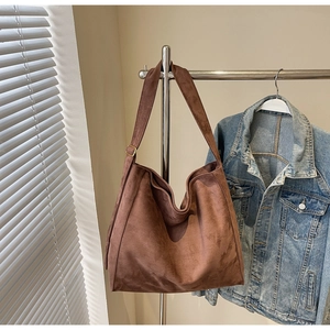 Borsa tote in pelle scamosciata marrone con tracolla larga appesa vicino a una giacca