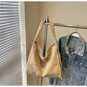 Dettaglio di una borsa tote in pelle scamosciata kaki con tracolla larga e giacca di jeans