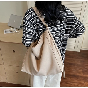 Dettaglio di una grande borsa tote beige minimalista indossata da una modella in scena