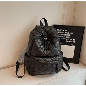 Detail of black quilted puffer backpack with mesh straps and woven zipper pulls
