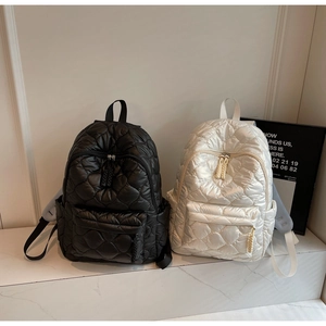 Close-up of quilted nylon mini backpacks in black and cream with woven zipper pulls