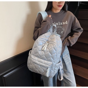 Close-up of light blue heart-quilted puffer backpack with front zipper pocket and side pockets
