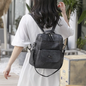 Outdoor shot of a black matte PU leather backpack worn by a model in a white dress