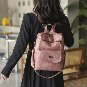 Rear view of a model wearing a large dusty rose PU leather backpack in a cozy cafe setting