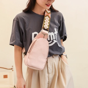 Detail of pink pebbled leather crossbody bag with geometric ethnic strap worn by a model