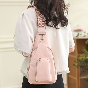 Close-up of light pink PU leather chest bag with patterned woven strap on a model