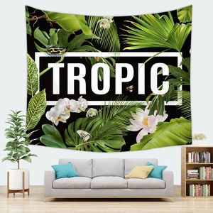 Dettaglio di un arazzo tropicale con foglie di monstera e testo TROPIC sopra un divano