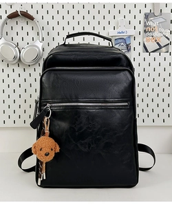 Detail of black pebbled leather backpack with silver zippers and a cute teddy bear charm