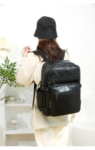 Rear view of a large black leather business backpack with multiple pockets on a model