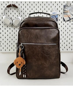 Detail view of a vintage dark brown leather backpack with multiple pockets and a dog charm