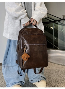 Detail of dark brown leather backpack with multiple pockets and cute teddy bear charm