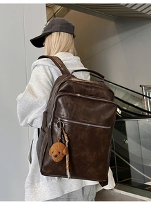 Detail of vintage brown multi-pocket backpack with silver zippers and plush bear charm