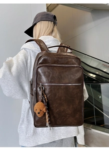 Brown leather backpack with plush charm worn by model in a modern urban lifestyle setting