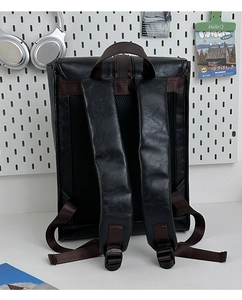 Detail of black PU leather backpack with brown padded straps on a white pegboard setup