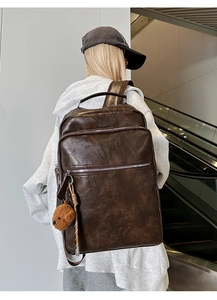 Detail of dark brown vintage backpack with multiple zippers and plush bear charm