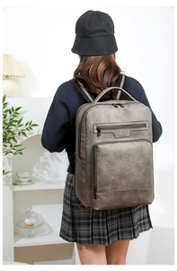 Deep grey PU leather backpack with multiple pockets shown on model in modern home setting
